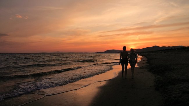 Due persone camminano su una spiaggia al tramonto.
