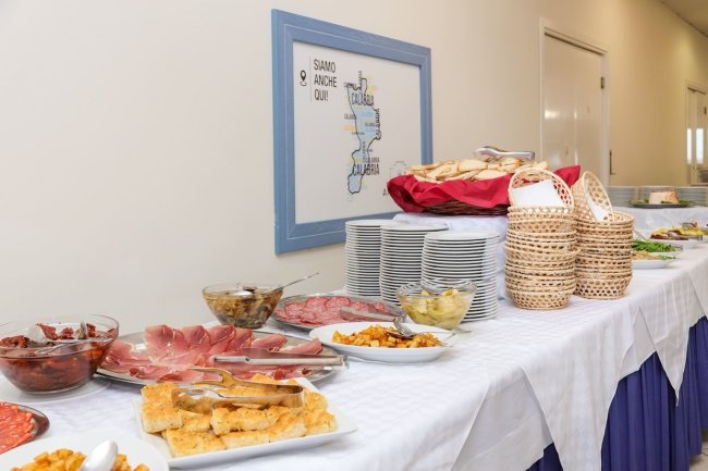 Buffet con salumi, formaggi e pane su una tovaglia bianca.