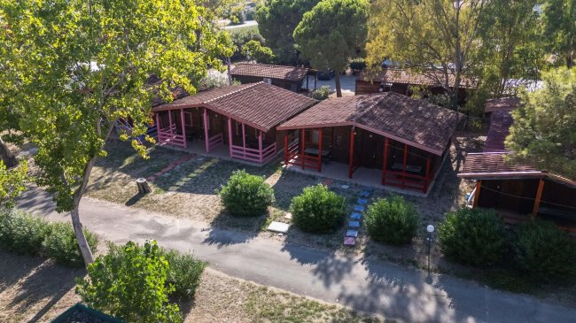 Complesso di bungalow con tetto a spiovente e portici, circondato da verde.