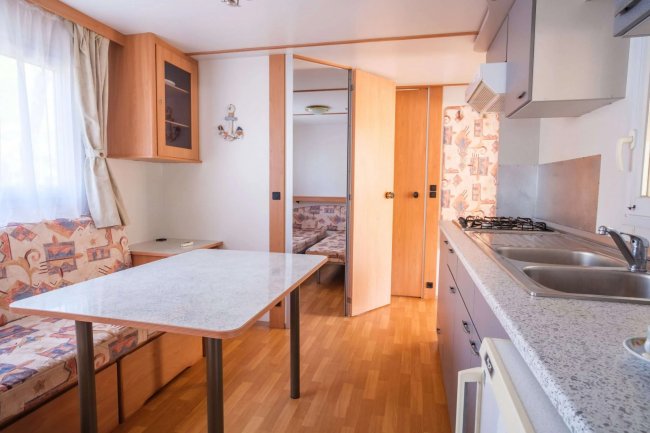 Cucina con tavolo, panca, piano cottura e lavello, porta verso altra stanza.