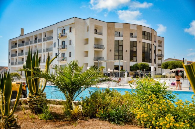 Un edificio moderno a più piani accanto a una piscina con piante verdi in primo piano.