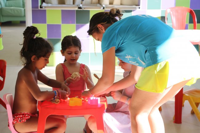 Bambini piccoli seduti a un tavolo rosso mentre fanno attività con un'animatrice.