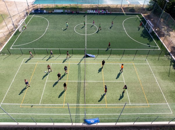 Campo sportivo con giocatori di calcio e pallavolo visti dall'alto.