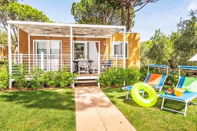 Una casa mobile con veranda e sedie a sdraio colorate in un giardino verde.