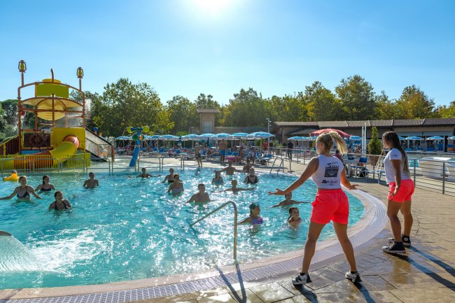 Persone che si divertono in una piscina con struttura per scivoli e animatori.