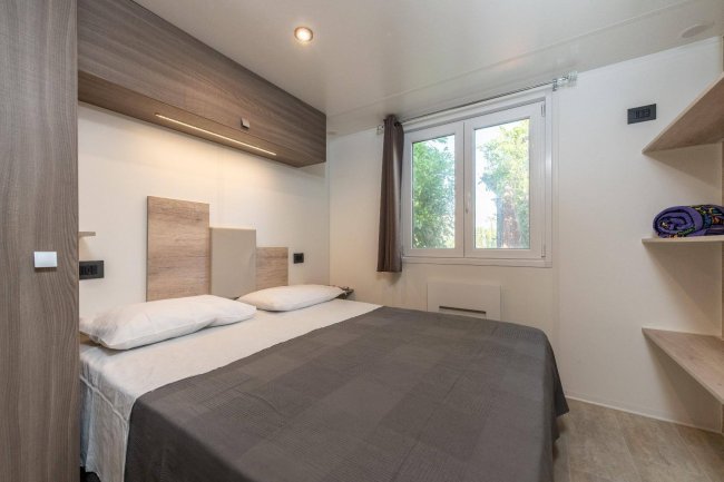 Interno di una camera da letto moderna con letto matrimoniale, finestra e scaffali.