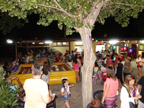 Folla di persone in un'area esterna con giochi gonfiabili sotto un albero.