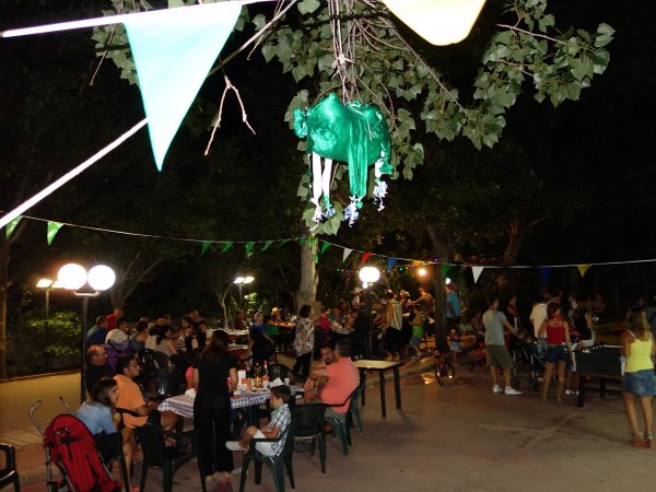 Festa serale all'aperto con tavoli, persone sedute e luci decorative.
