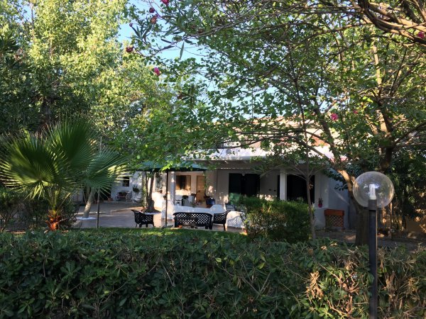 Una casa immersa nel verde con tavoli all'esterno e piante rigogliose.