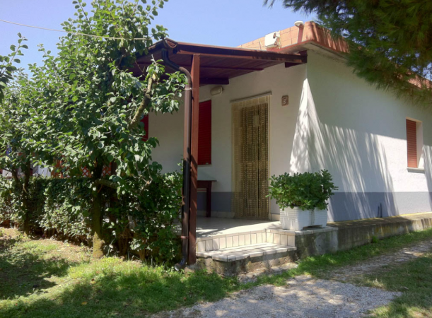 Casa bianca con tetto rosso, ingresso coperto, piante lungo il vialetto.