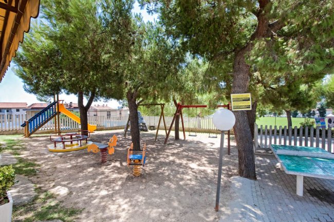 Un'area giochi all'aperto con altalene, scivoli e alberi ombrosi.