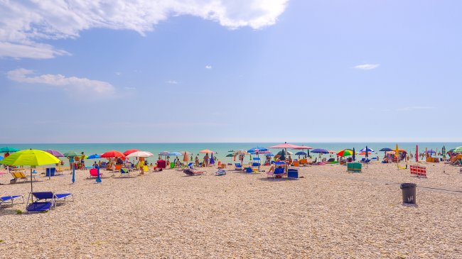 Spiaggia con ciottoli, ombrelloni colorati e mare calmo.