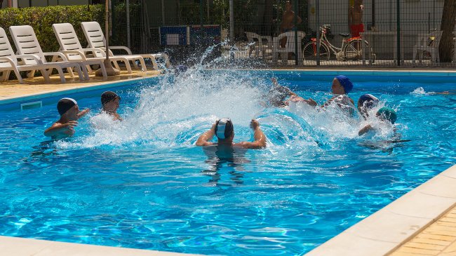 Persone che giocano in una piscina, creando schizzi d'acqua.
