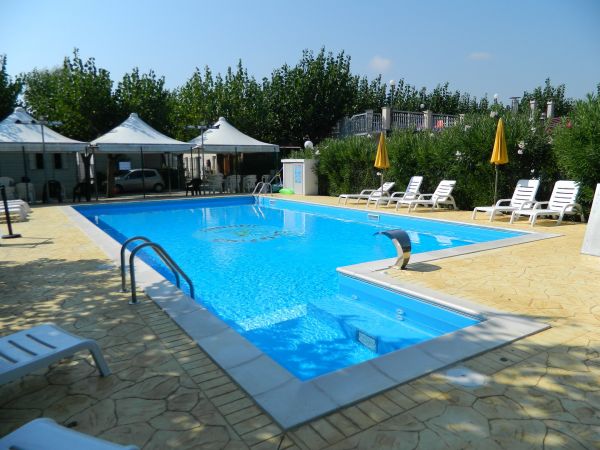 Piscina all'aperto con sedie a sdraio bianche, ombrelloni gialli e vegetazione circostante.