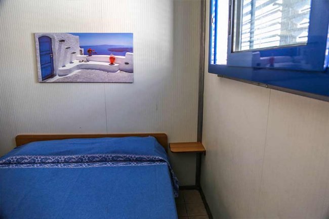 Una stanza con letto blu e un quadro di paesaggio marino sopra.