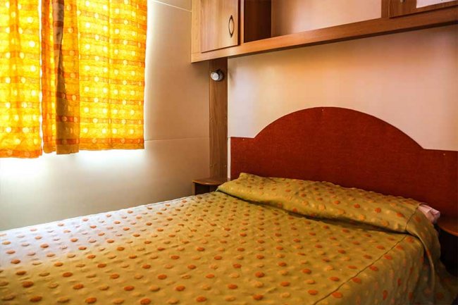 Una camera con letto ed elegante copriletto arancione a pois. Tende gialle filtrano la luce.