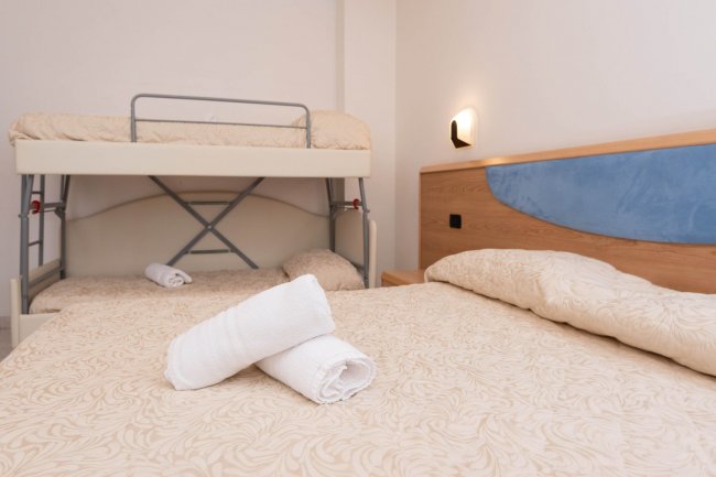 Stanza con letto matrimoniale, letto a castello e asciugamani piegati.