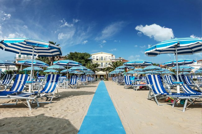 Spiaggia con sdraio e ombrelloni blu a righe.