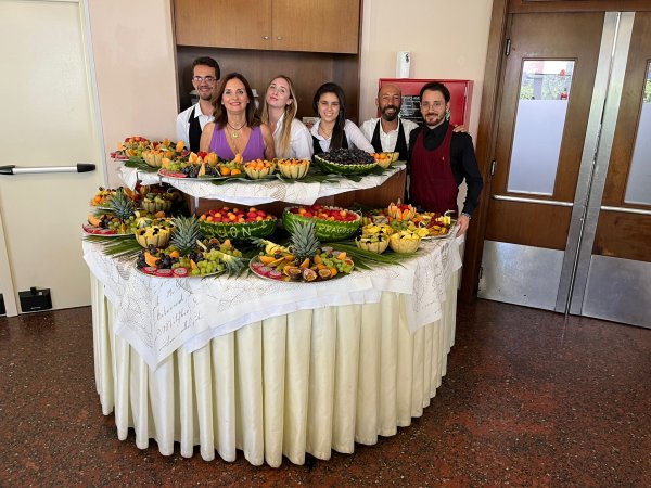 Sei persone posano dietro un tavolo ricco di frutta decorata.