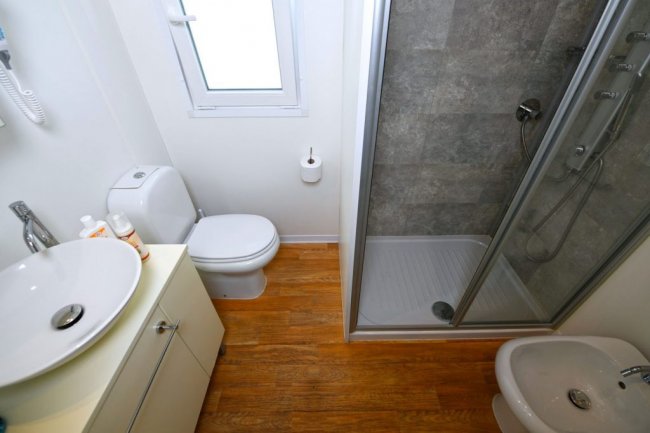 Un bagno con box doccia, lavabo, WC e bidet. Pavimento effetto legno.