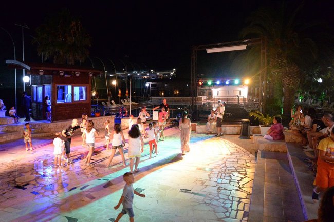 Serata all'aperto con bambini e adulti che ballano sotto luci colorate.