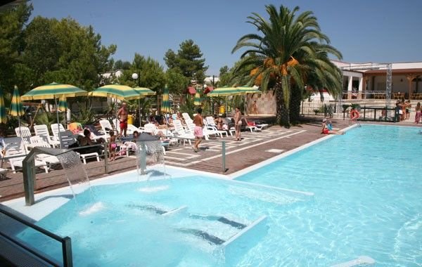 Piscina all'aperto con lettini e ombrelloni verdi e gialli.