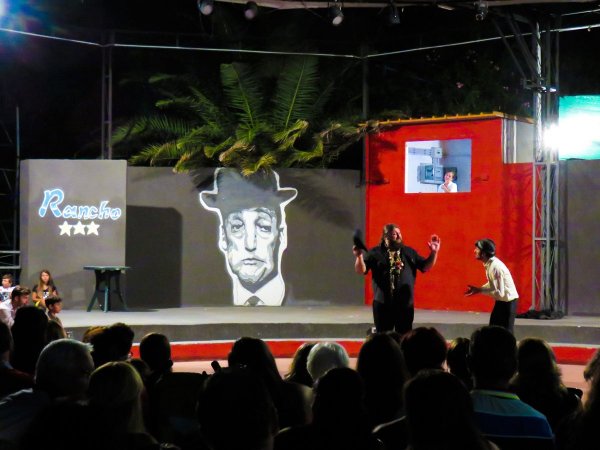 Spettacolo teatrale all'aperto con pubblico e scenografia colorata.