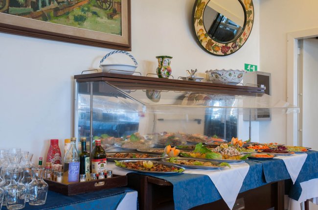 Buffet con piatti assortiti, bottiglie di condimenti e bicchieri su una tovaglia blu.