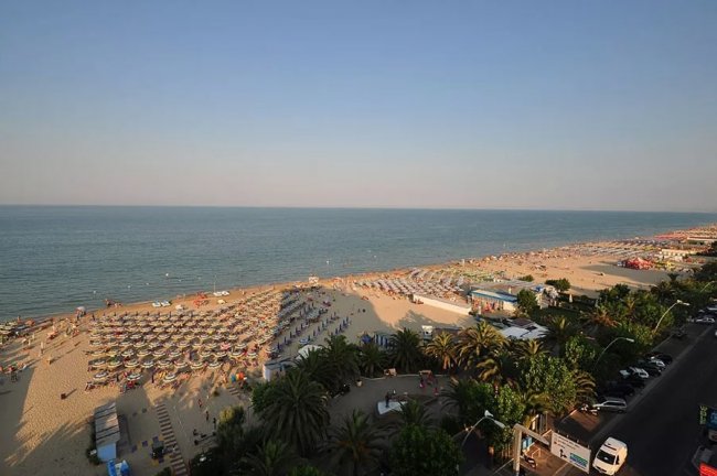 Vista aerea di una spiaggia affollata con ombrelloni e mare calmo.