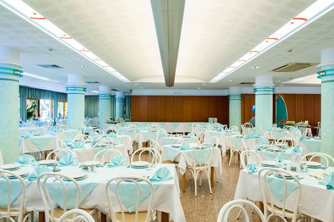 Sala da pranzo con tavoli apparecchiati e sedie bianche.