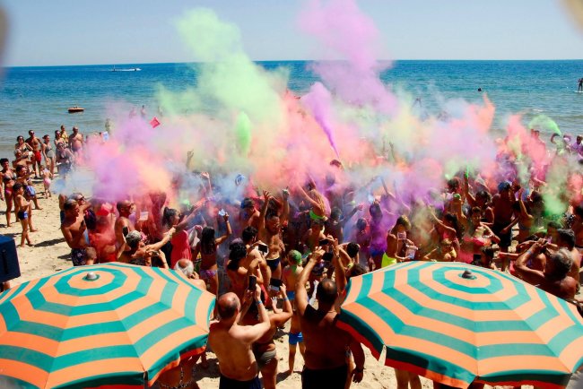 Festa colorata sulla spiaggia con persone e ombrelloni arancioni e verdi.