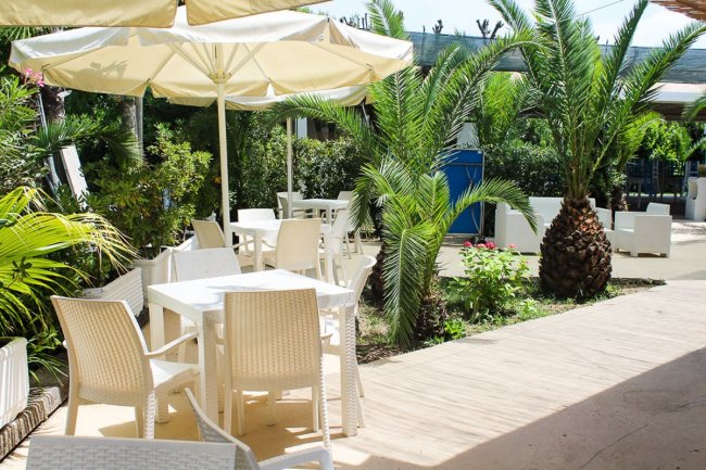 Tavoli con sedie bianche all'aperto, ombrelloni gialli e piante tropicali.