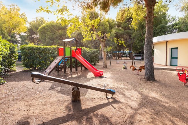 Parco giochi con altalena e scivolo rosso.