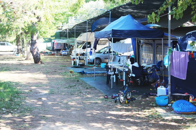 Area campeggio con auto, tende, tavoli e giocattoli per bambini.