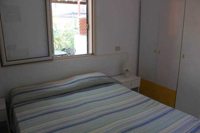 Camera da letto con un letto a righe blu e armadio bianco, finestra aperta.