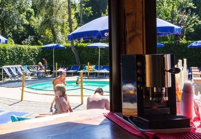 Piscina esterna con ombrelloni blu e macchina da caffè in primo piano.