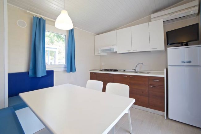 Cucina moderna con tavolo bianco, sedie, divano blu, e mobili in legno e bianco.
