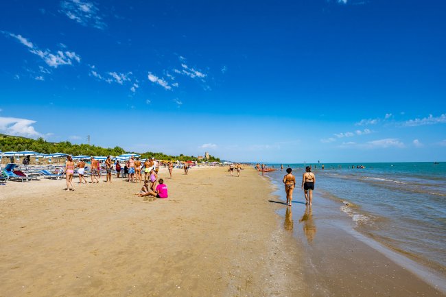 Una spiaggia affollata con persone che camminano lungo la riva sotto un cielo blu.