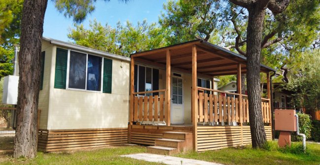 Casa mobile con veranda in legno circondata da alberi.
