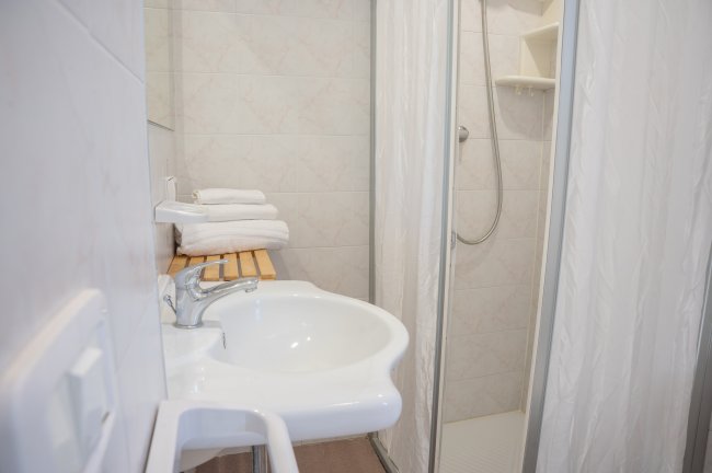Bagno con lavabo, doccia e asciugamani su una mensola.
