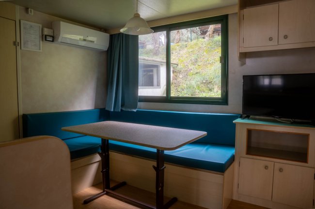 Sala con tavolo, sedute blu, finestra, TV e condizionatore.