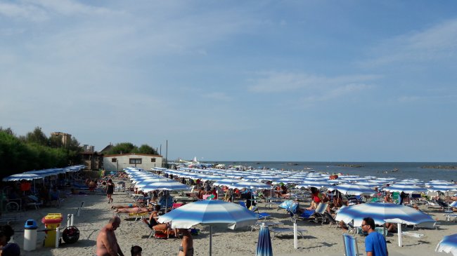 Spiaggia con ombrelloni blu e bianchi, molte persone presenti.