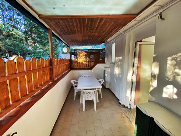 Una terrazza coperta con tavolo bianco e sedie di plastica, recintata in legno.