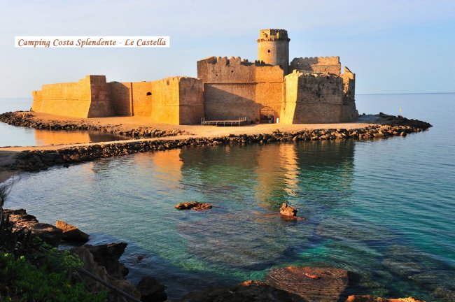 Un castello sul mare al tramonto, circondato da acqua cristallina.