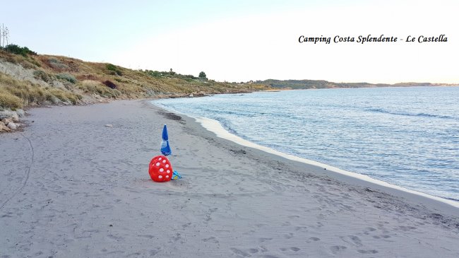 Spiaggia sabbiosa con ombrelloni e pallone rosso. Campeggio Costa Splendente sullo sfondo.