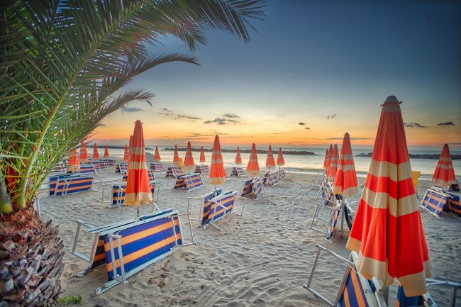 Spiaggia all'alba con ombrelloni a righe arancioni e blu.