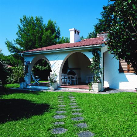 Casa con portico e tavolo da esterno, circondata da prato e alberi.