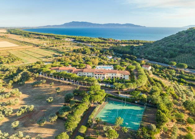 Vista aerea di un resort con campi da tennis vicino al mare.
