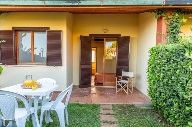 Terrazza con tavolo bianco e sedie. Vista su porta aperta e persiane marroni.