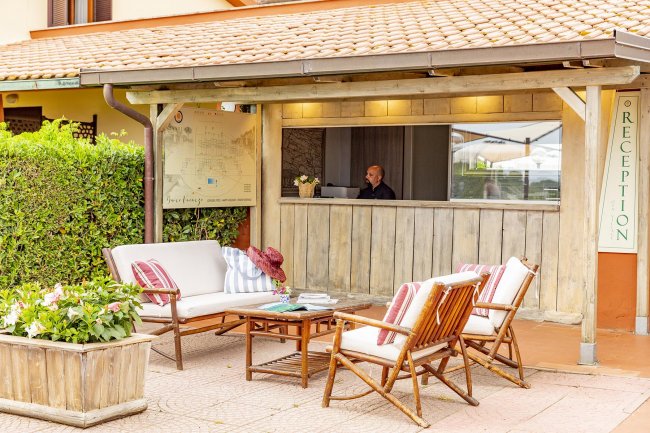 Esterno di una reception con mobili da giardino in legno e cartello di benvenuto.